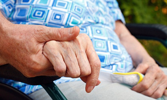 Närbild på en äldre hand hos en person som sitter i rullstol och håller en yngre hand