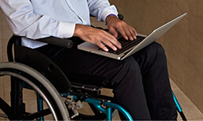 Bild på person som sitter i rullstol med en bärbar dator i knät.