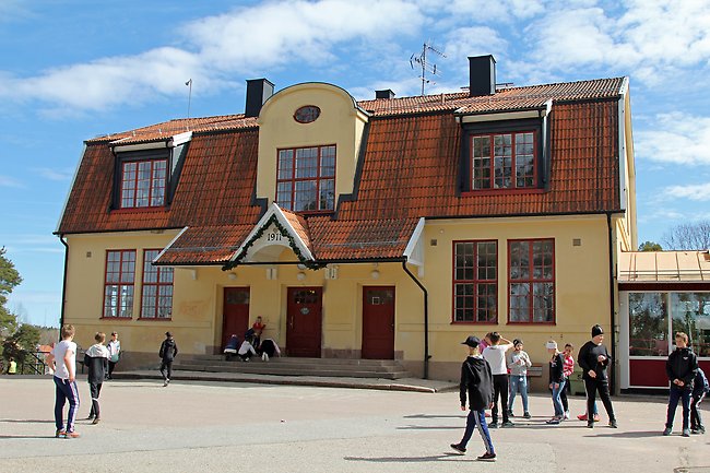 Den äldre skolbyggnaden på västanbyskolan har gul fasad och är i två våningar framför skolan syns elever på skolgården