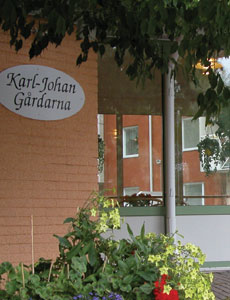 Tegelvägg med skylt Karl-Johan Gårdarna. Framför väggen finns blommor i en rabatt