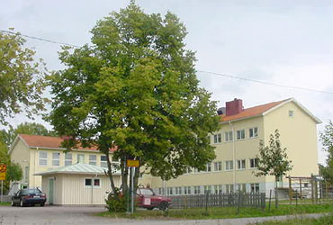 Sätra skola ligger i ett ljusgul byggnad i tre våningar med rött tak. Framför byggnaden syns ett stort träd.