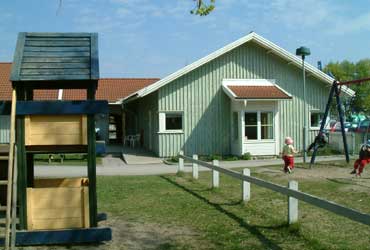 Grön enplansbyggnad vid Pinnhagens förskola med lekredskap framför huset.