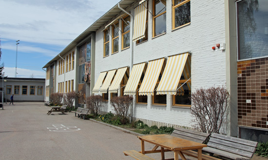 Jernvallsskolan ligger i en tvåvångingsbyggnad med ljusgrå tegelfasad. På några av fönstrena är gula markiser utfällda. Framför skolan en asfaltsyta.