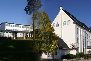 Fotomontage med två byggnader på Murgårdskolan. Den framträdande byggnaden på bilden är fyra våningar hög med sadeltak och vit fasad. Byggnaden i bakgrunden är också vit men med ett plattare tak.