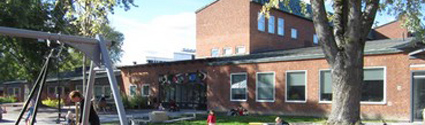 Entré till Kulturförskolan Flygande draken som ligger i en rödfärgad tegelbyggnad. Framför huset en stor lekplats och träd