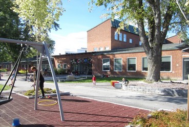 Entré till Kulturförskolan Flygande draken som ligger i en rödfärgad tegelbyggnad. Framför huset en stor lekplats och träd