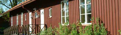 Trollstugans förskola ligger i ett rött hus med buskar framför.