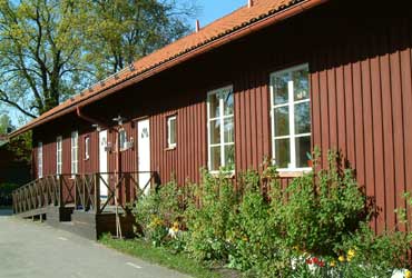 Trollstugans förskola ligger i ett rött hus med buskar framför.
