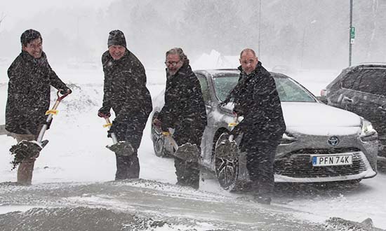 Fyra personer står bredvid varandra i snöoväder. De håller i varsin spade. 