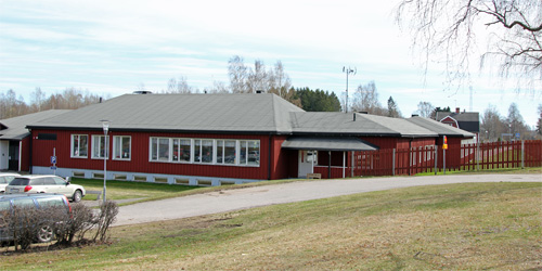 Kungsgårdens skola är en röd enplansbyggnad med ljusgrått tak. Runt skolan finns gräsytor.