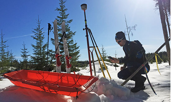 En mätningsingenjör i svarta kläder mäter marken i snöigt landskap.