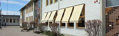 Gråvit tvåplans tegelbyggnad vid Jernvallsskolan med gula markiser nedfällda för fönstren