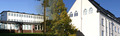 Fotomontage av två vita byggnader vid Murgårdsskolan. Vid husen finns några tallar