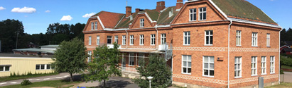 Österfärnebo skolas röda tegelbyggnad i tre våningar. Framför skolan finns några träd.