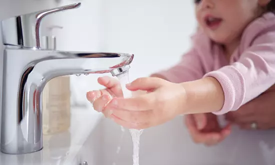 Närbild på ett litet barn som tvättar händerna under en vattenkran.