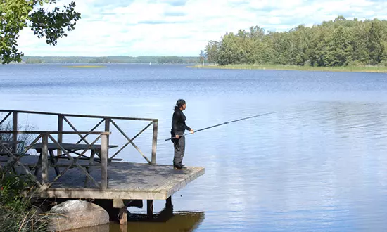 Kvinna fiskar på en brygga vid en sjö. Foto.