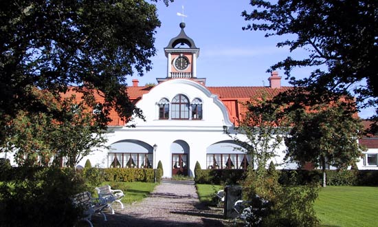 Orangeriet i Gysinge är en vit byggnad i två våningar. På taket finns ett torn med en urtavla. Framför byggnade en lummig park med stora träd och planteringar