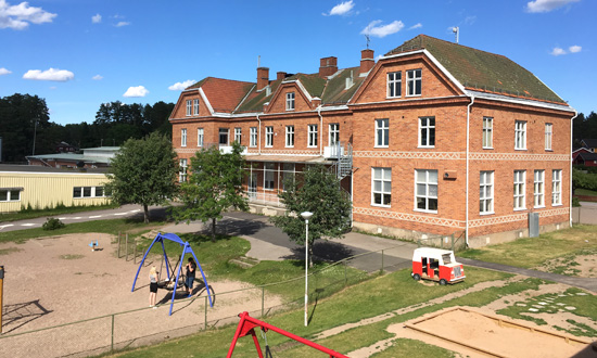 Österfärnebo skola ligger i en äldre trevåningsbyggnad med röd fasad. Framför byggnaden syns gräsytor varvat med grusytor och lekredskap.