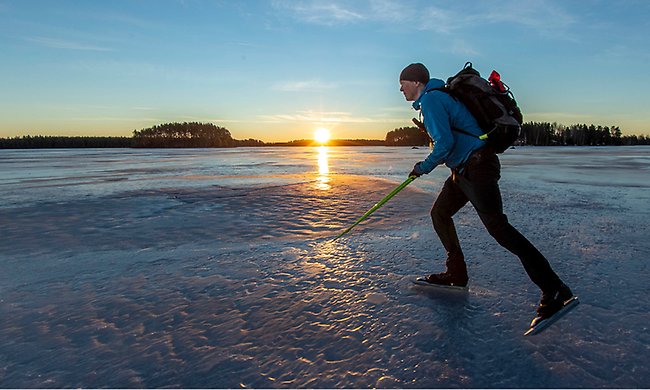 Vinter med is på Storsjön i solnedgång. En person i blåkläder åker längdskidor över isen. 