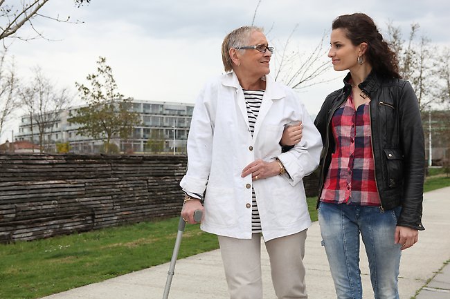 En äldre kvinna med käpp är på promenad med en yngre kvinna som ledsagare.