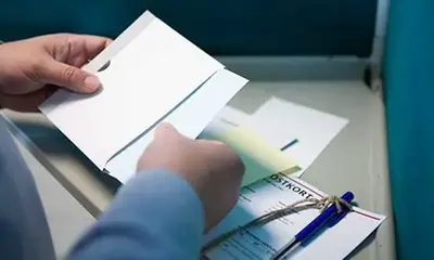 Person som stoppar valsedel i kuvert i röstningsbåset
