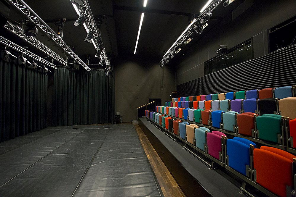 Publikplatser med olikfärgade stolar på gradängen. I taket blanka belysningramper