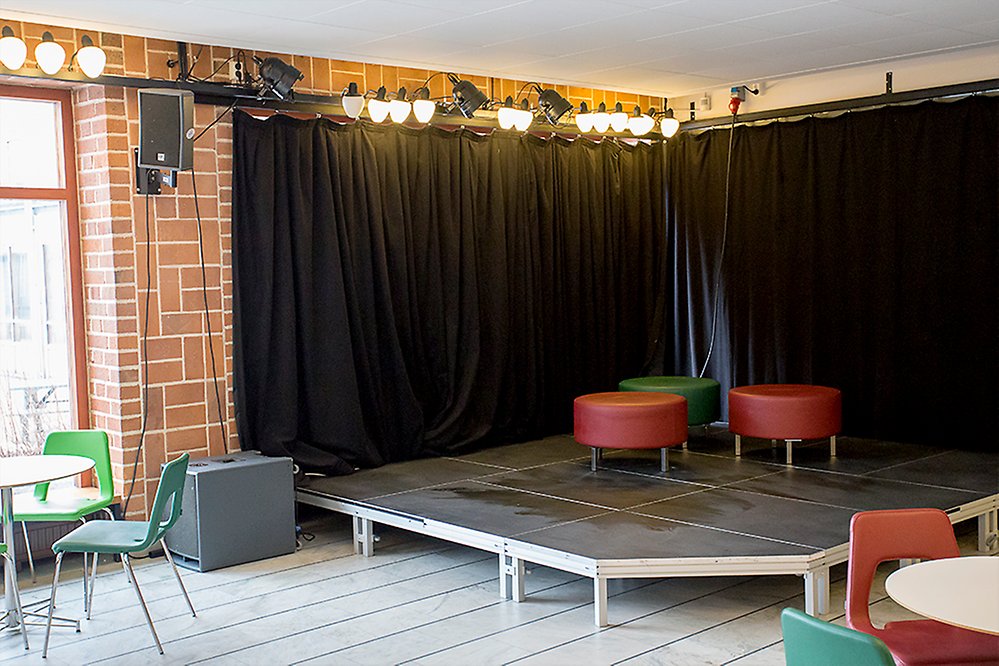 Scenyta i foajén med svart draperi bakom scenen. På scenen finnns några röda och gröna runda sittmöbler.